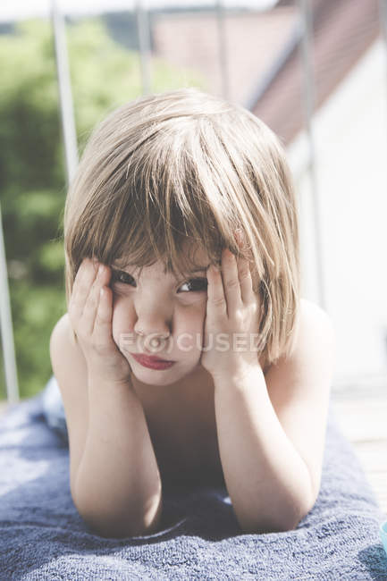 Retrato de una niña triste tumbada sobre una toalla en el balcón - foto de stock