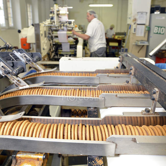 Lignes de production avec biscuits dans une usine de cuisson avec des travailleurs sur fond — Photo de stock