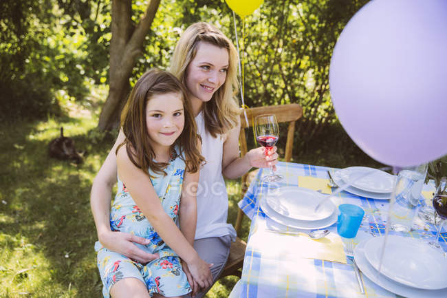 Daughter sitting on mother's lap at garden party table — Stock Photo