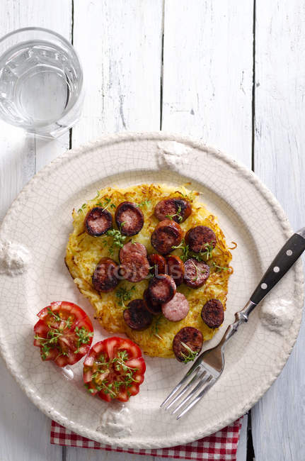 Plate of potato roesti garnished with slices minced pork sausage and tomatoes — Stock Photo