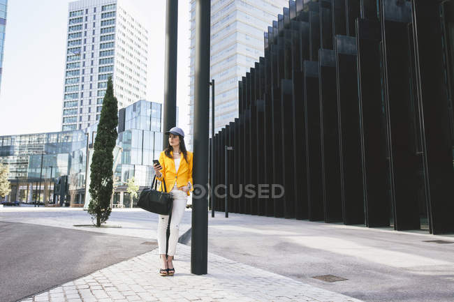 Spanien, Katalonien, Barcelona, junge moderne Frau mit gelber Jacke lehnt an Straßenlaterne — Stockfoto