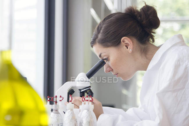 Retrato de una joven química que mira a través del microscopio - foto de stock