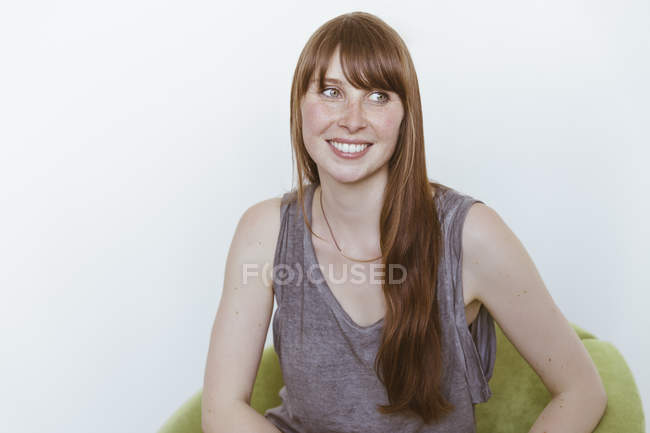 Retrato de mulher sorridente sentada em cadeira macia na frente do fundo branco — Fotografia de Stock