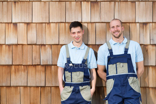 Due artigiani al muro di legno sorridenti alla macchina fotografica — Foto stock