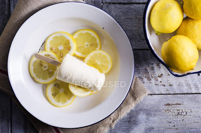 Bowl of lemons and plate of home-made lemon cream ice lolly on lemon slices, elevated view — Stock Photo