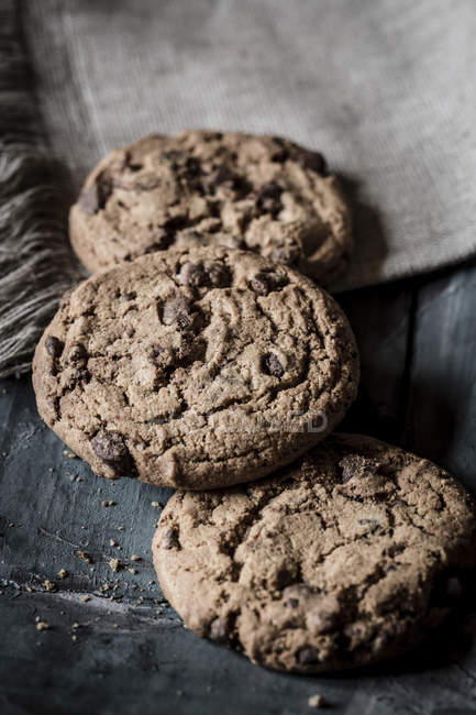 Three chocolate cookies and cloth on grey wood — Stock Photo