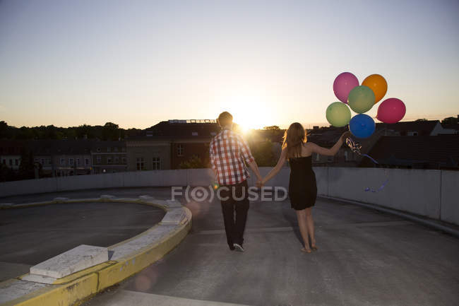 Pareja adolescente caminando con globos en rampa de aparcamiento - foto de stock