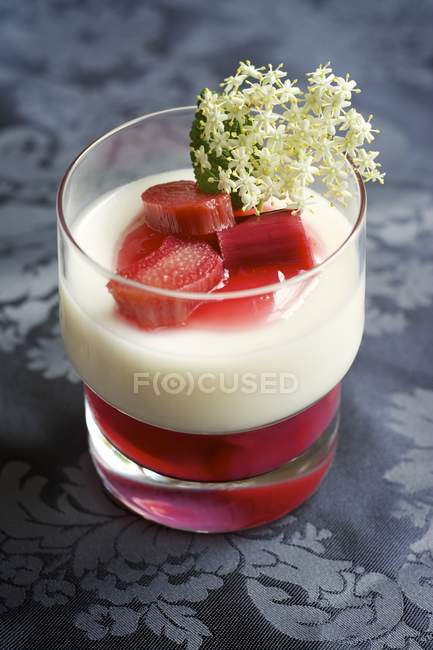 Glass of panna cotta and rhubarb coulis garnished with elderflower — Stock Photo