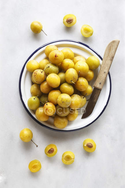 Bowl of mirabelles and a kitchen knife on white background — Stock Photo