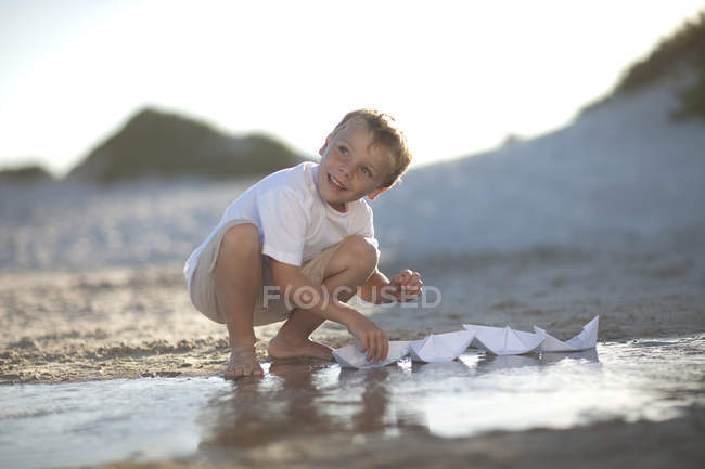 Хлопчик грає з паперу човни на воді басейну на піщаному пляжі — стокове фото
