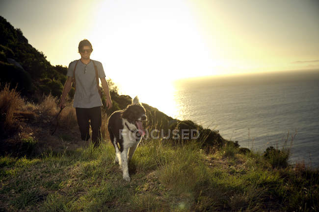 Mann spaziert mit Hund in der Abenddämmerung an der Küste entlang — Stockfoto