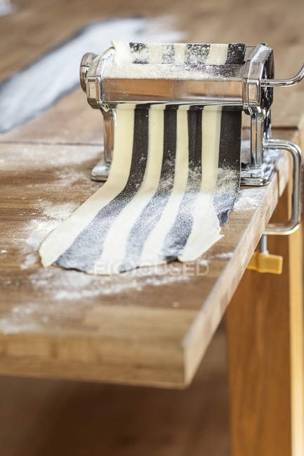 Making striped pasta in pasta machine, partly colored with cuttlefish ink — Stock Photo