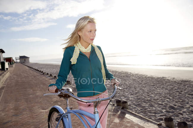 Lächelnde junge Frau mit Fahrrad an der Strandpromenade — Stockfoto