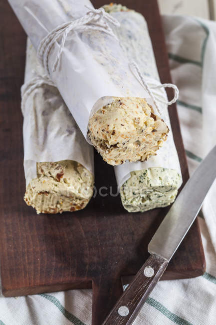 Three rolls of differently flavoured compound butters on chopping board — Stock Photo