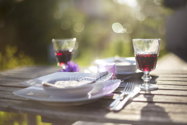 Tavolo da giardino coricato con due bicchieri di vino rosso retroilluminato — Foto stock