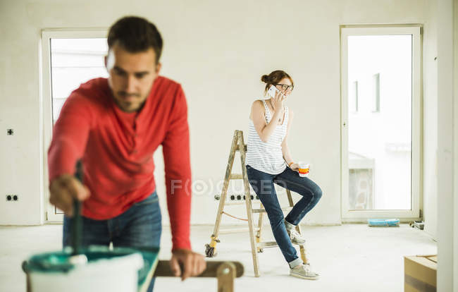 Mujer joven en el teléfono con el hombre pintando tablero de madera en primer plano - foto de stock