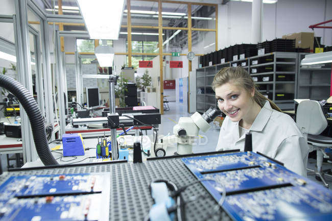 Retrato del técnico sonriente examinando la placa de circuito con microscopio - foto de stock