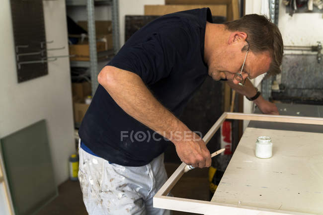 Fabricante de marcos en taller pintando un marco de madera - foto de stock