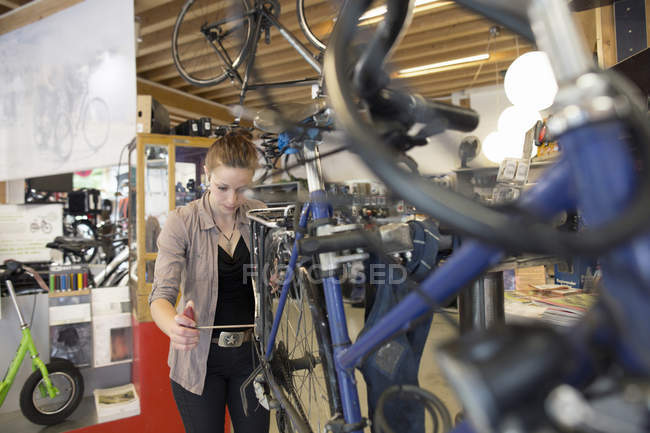 Giovane donna che lavora in un negozio di riparazione di biciclette — Foto stock