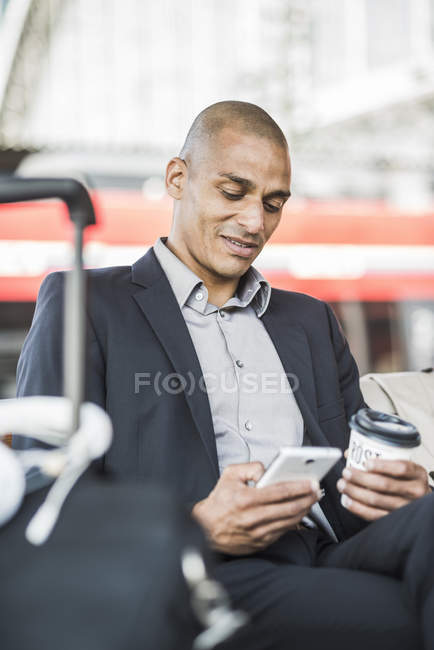 Uomo d'affari alla stazione ferroviaria in cerca di smartphone — Foto stock