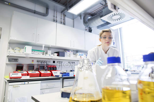 Jeune femme scientifique travaillant dans un laboratoire biologique cherchant une bouteille — Photo de stock