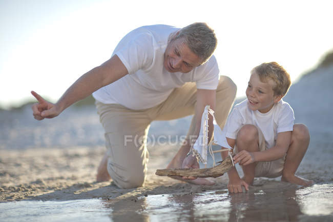 Батько і син, граючи з іграшкою човен в басейн з водою на піщаний пляж — стокове фото