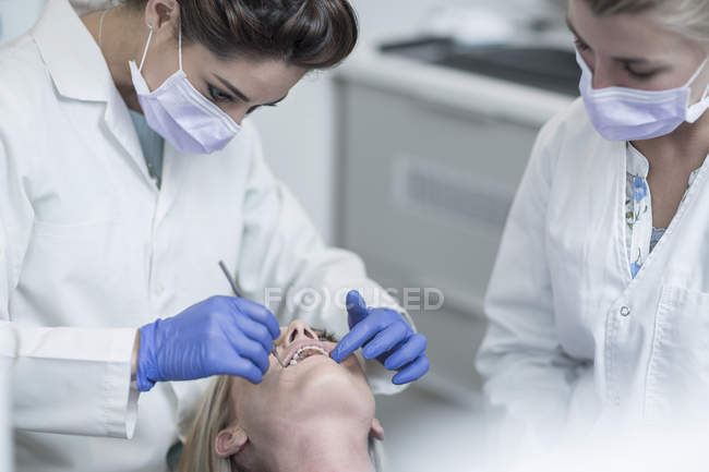 Female dentist examining patient with mouth mirror — Stock Photo