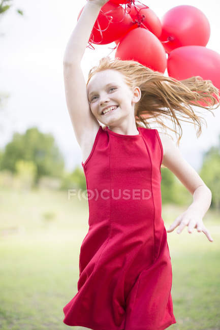 Portrait of running girl with red balloons wearing red dress — Stock Photo