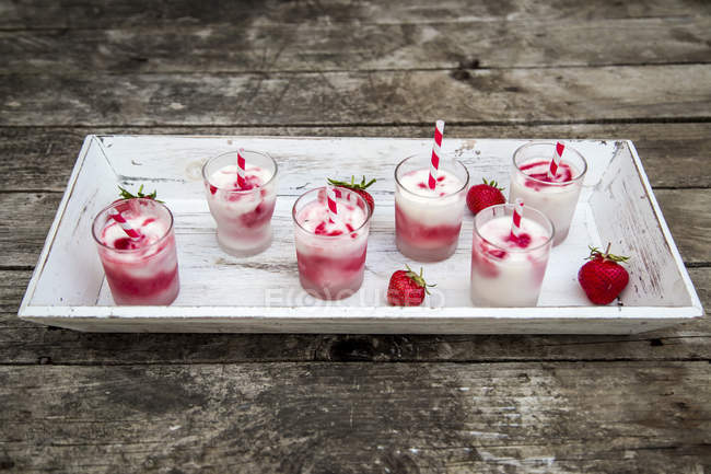 Erhöhte Ansicht von sechs Gläsern Erdbeer-Buttermilch-Eis mit Trinkhalmen und frischen Erdbeeren auf Tablett — Stockfoto