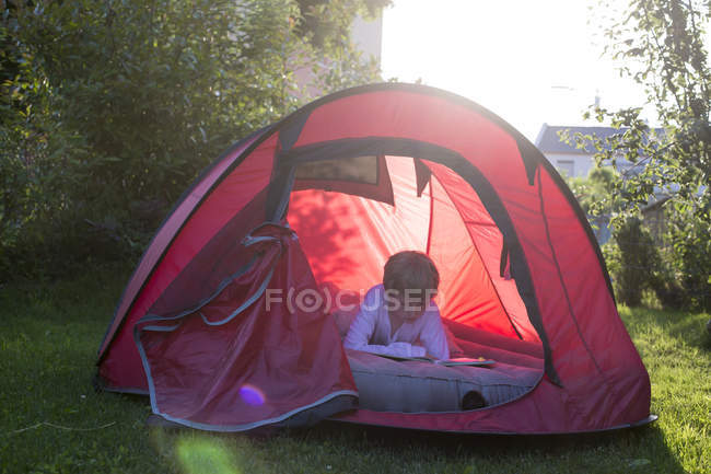 Junge liest in einem roten Zelt in der Abenddämmerung — Stockfoto