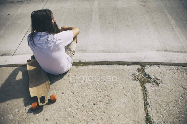 Vue aérienne de l'homme de type Hipster avec un longboard assis sur le trottoir — Photo de stock