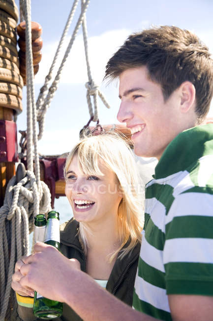 Felice giovane uomo e donna clinking bottiglie di birra su un veliero — Foto stock