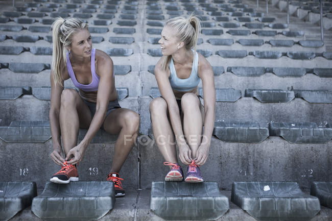 Deux sportives assises sur la tribune d'un stade attachant des chaussures — Photo de stock