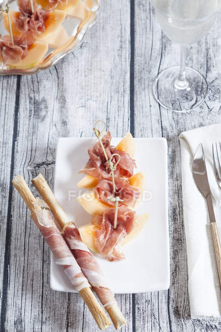 Plate of Charentais melon slices with ham and Grissini wrapped with ham — Stock Photo
