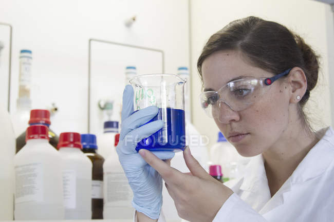 Портрет молодої жінки-хіміка, що тримає Бейкера з блакитною рідиною — стокове фото