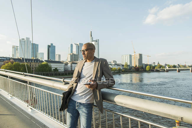 Germany, Frankfurt, businessman on bridge with briefcase and smartphone — Stock Photo