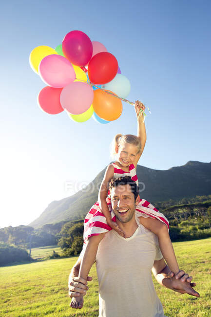 Счастливый отец носит дочь с воздушными шарами на плечах — стоковое фото