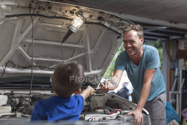 Hijo ayudando a padre en casa garaje trabajando en el coche — Ayudas,  enseñanza - Stock Photo | #181528374