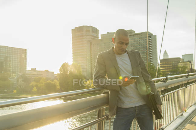 Германия, Франкфурт, бизнесмен на мосту смотрит на смартфон — стоковое фото