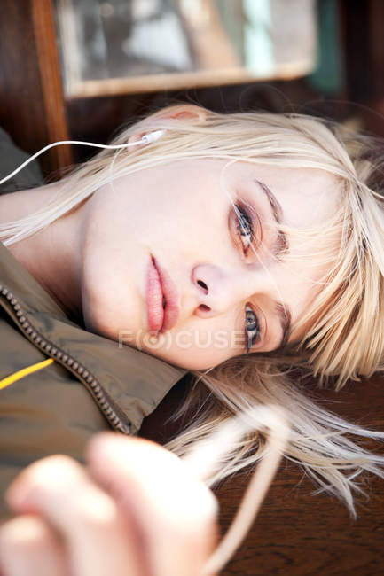 Relaxado jovem deitado em um banco ouvindo música — Fotografia de Stock