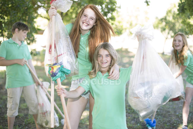 Посміхаються діти, піднімаючи сміття в парку — стокове фото