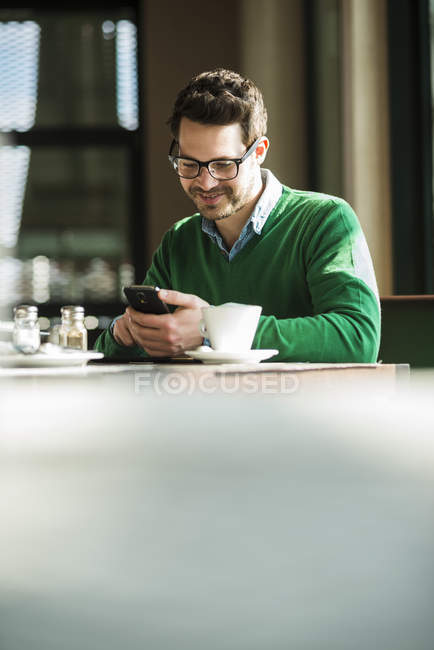 Mann sitzt in Café und benutzt Handy — Stockfoto