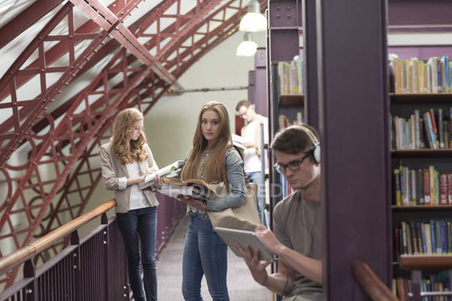 Estudantes em uma biblioteca entre prateleiras de livros — Fotografia de Stock