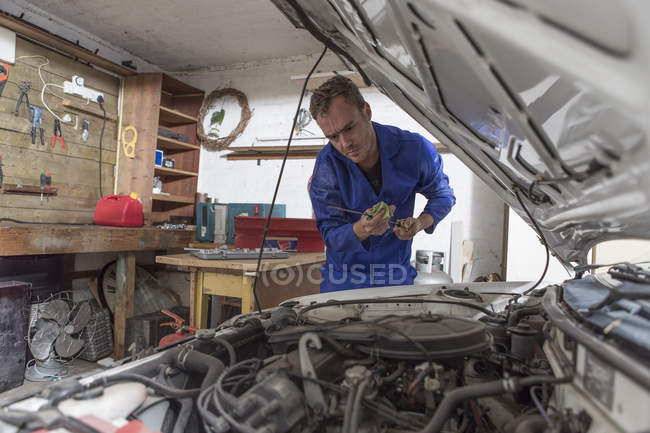 Man working on car in home garage looking at dipstick — diy, hobby - Stock  Photo | #181531510