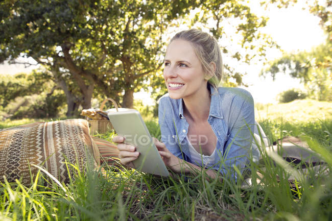 Donna sorridente con tablet digitale sdraiata sul prato — Foto stock