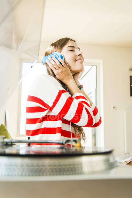 Giovane donna a casa con le cuffie che ascolta musica dal giradischi — Foto stock