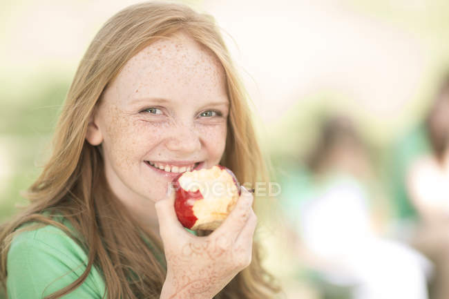 Porträt eines lächelnden Mädchens mit roten Haaren, das einen Apfel isst — Stockfoto