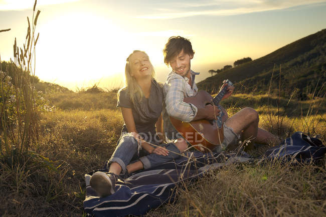Feliz joven pareja con guitarra en manta en el prado - foto de stock
