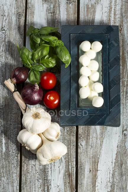 Верхний вид сыра Моцарелла, помидоры, чеснок, базилик и лук на деревянный стол — стоковое фото