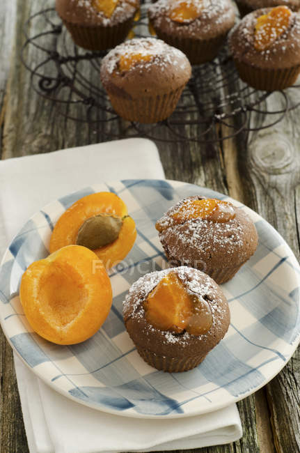 Chocolate muffins on cooling rack with apricot on wooden table — Stock Photo
